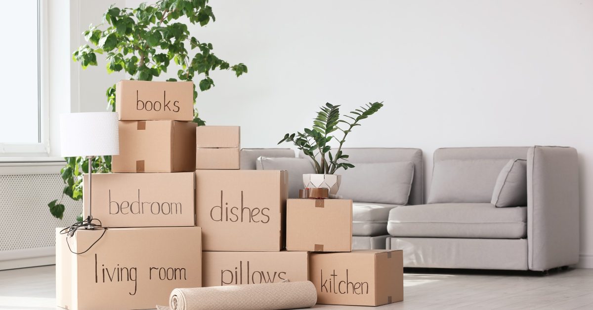 A stacked pile of packed and labeled cardboard boxes of various sizes with a grey couch in the background.